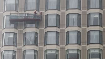 Pekerja membersihkan jendela gedung bertingkat di Kawasan Bundaran Hotel Indonesia (HI), Jakarta Pusat, Sabtu (12/2/2022). [Suara.com/Alfian Winanto]