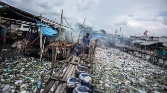 Warga memikul jeriken air melintasi jembatan kayu di antara sampah di kawasan perkampungan nelayan Cilincing, Jakarta Utara, Minggu (20/2/2022). [ANTARA FOTO/Aprillio Akbar/tom]