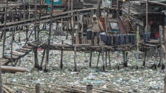 Warga memikul jeriken air melintasi jembatan kayu di antara sampah di kawasan perkampungan nelayan Cilincing, Jakarta Utara, Minggu (20/2/2022). [ANTARA FOTO/Aprillio Akbar/tom]