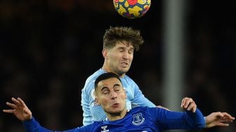 Gelandang Everton Anwar El Ghazi (bawah) dan bek Manchester City John Stones (atas) melompat untuk menyundul bola saat pertandingan sepak bola Liga Premier Inggris antara Everton dan Manchester City di Stadion Goodison Park, Inggris, Sabtu (26/2/2022). [Oli SCARFF / AFP]