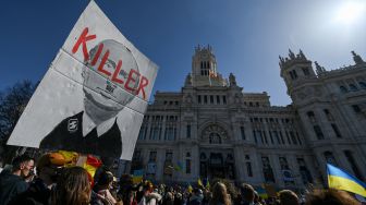 Seorang pengunjuk rasa memegang poster bergambar Presiden Rusia Vladimir Putin dengan tulisan "Pembunuh" saat memprotes invasi Rusia ke Ukraina ddi depan Istana Cibeles, Madrid, Spanyol, Minggu (27/2/2022). [GABRIEL BOUYS / AFP]
