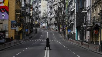 Seorang warga sipil melintasi jalan kosong di pusat kota Kyiv, Ukraina, Minggu (27/2/2022). [Aris Messinis / AFP]