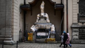 Warga berjalan melewati patung-patung bersejarah yang dibungkus di Archcathedral Basilica of the Assumption of the Blessed Virgin Mary atau Katedral Latin di Lviv, Ukraina, Sabtu (5/3/2022). [Daniel LEAL / AFP]  