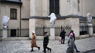 Warga berjalan melewati patung-patung bersejarah yang dibungkus di Archcathedral Basilica of the Assumption of the Blessed Virgin Mary atau Katedral Latin di Lviv, Ukraina, Sabtu (5/3/2022). [Daniel LEAL / AFP] 