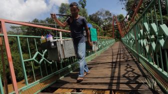 Seorang pedagang berjalan melintasi Jembatan Wiratman, Kelurahan Srengseng Sawah, Jakarta, Sabtu (12/3/2022). [Suara.com/Angga Budhiyanto]