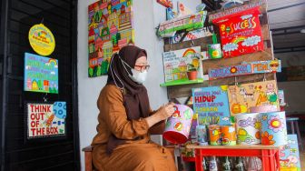 Lani Cahyaningsari (48) menyelesaikan pembuatan kerajinan lukis di atas media kaleng bekas di Kaleng Lani, Depok, Jawa Barat, Minggu (13/3/2022). [Suara.com/Septian]