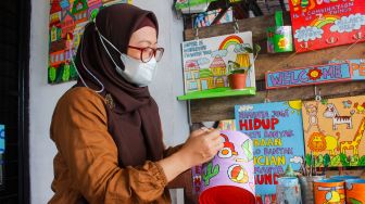 Lani Cahyaningsari (48) menyelesaikan pembuatan kerajinan lukis di atas media kaleng bekas di Kaleng Lani, Depok, Jawa Barat, Minggu (13/3/2022). [Suara.com/Septian]