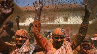 Para janda yang berlumuran Gulal (bubuk warna) menari saat mereka berpartisipasi dalam perayaan Holi di sebuah kuil di Vrindavan, India, Selasa (15/3/2022). [Money SHARMA / AFP]