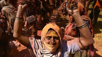 Seorang janda yang berlumuran Gulal (bubuk warna) menari saat mereka berpartisipasi dalam perayaan Holi di sebuah kuil di Vrindavan, India, Selasa (15/3/2022). [Money SHARMA / AFP]