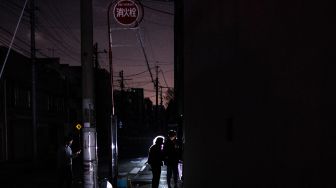 Orang-orang berjalan di sepanjang jalan area perumahan saat pemadaman listrik yang berlangsung setelah gempa berkekuatan 7,3 SR mengguncang wilayah Jepang Timur di Tokyo, Jepang, Kamis (17/3/2022). [Philip FONG / AFP]