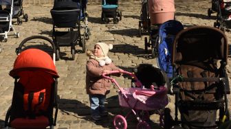 Ratusan kereta dan keranjang bayi kosong di pajang di luar gedung dewan kota di Lviv, Ukraina, Jumat (18/3/2022). [Yuriy Dyachyshyn / AFP]
