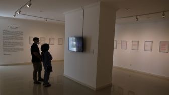 Pengunjung mengamati karya seni instalasi video dalam pameran tunggal karya Otty Widasary yang bertajuk "Partisan" di Gedung D, Galeri Nasional, Jakarta, Minggu (20/3/2022). [Suara.com/Angga Budhiyanto]