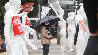 Seorang aktivis mengenakan masker bertanda silang berdiri disamping manekin saat melakukan aksi di depan Polda Metro Jaya, Jakarta Selatan, Senin (21/3/2022). [Suara.com/Alfian Winanro]