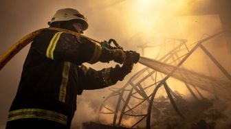 Petugas pemadam kebakaran memadamkan api di gudang yang terbakar akibat dihantam rudal Rusia di pinggiran kota Kyiv, Ukraina, kamis (24/3/2022). [FADEL SENNA / AFP]
