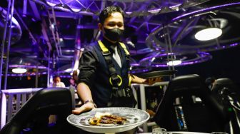 Pelayan menyajikan makan malam diatas ketinggian 50 meter di restoran Lounge In The Sky Indonesia di Setiabudi, Jakarta Selatan, Selasa (29/3/2022). [Suara.com/Alfian Winanto]