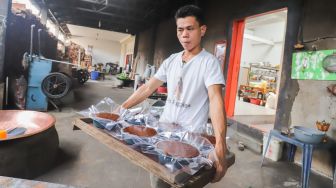 Pekerja membawa dodol betawi yang sudah ditaruh dalam wadah untuk didinginkan di rumah produksi Dodol Betawi Sari Rasa Ibu Yuyun, Jakarta Selatan, Kamis (31/3/2022). [Suara.com/Alfian Winanto]