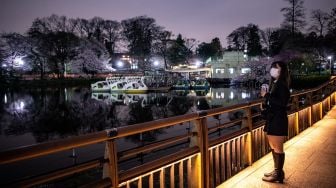 Seorang wanita melihat bunga sakura yang bermekaran di Taman Inokashira, Tokyo, Jepang, Rabu (30/3/2022). [Philip FONG / AFP]