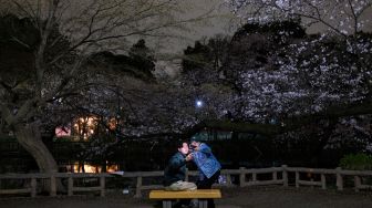 Pasangan melihat bunga sakura yang bermekaran di Taman Inokashira, Tokyo, Jepang, Rabu(30/3/2022). [Philip FONG / AFP]