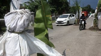 Pengendara sepeda motor melintas di jalan rusak yang ditanami tanaman pisang dan tebu di Desa Janti, Kediri, Jawa Timur, Sabtu (2/4/2022). [ANTARA FOTO/Prasetia Fauzani/foc]