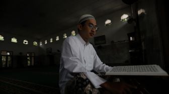 Pengurus Masjid Jami Maulana Hasanuddin, Fachrie Aie (30) membaca ayat suci Al-Qur'an di dalam area masjid, Cikoko, Pancoran, Jakarta, Minggu (3/4/2022). [Suara.com/Angga Budhiyanto]