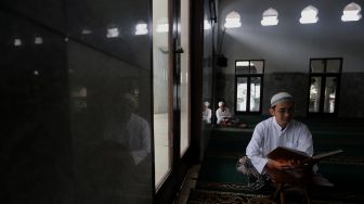 Pengurus Masjid Jami Maulana Hasanuddin, Fachrie Aie (30) membaca ayat suci Al-Qur'an di dalam area masjid, Cikoko, Pancoran, Jakarta, Minggu (3/4/2022). [Suara.com/Angga Budhiyanto]