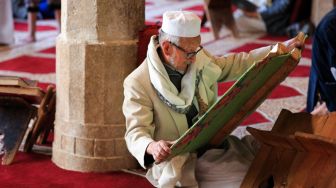 Seorang pria Muslim membaca Alquran di Masjid Al-Kabir, Sana'a, Yaman, Sabtu (2/4/2022). [MOHAMMED HUWAIS / AFP]
