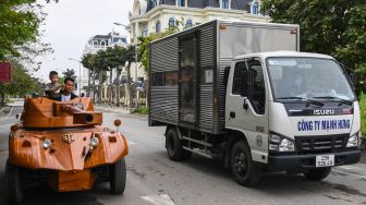 Truong Van Dao dan putranya mengendarai tank kayu yang terbuat minibus tua di sebuah daerah perumahan di provinsi Bac Ninh, Vietnam, Senin (28/3/2022). [Nhac NGUYEN / AFP]