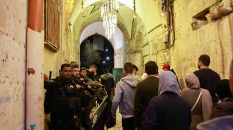 Pasukan keamanan Israel berjaga-jaga ketika warga Palestina berjalan di jalan di Kota Tua Yerusalem, Sabtu (2/4/2022). [Menahem KAHANA / AFP]