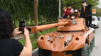 Anak-anak sekitar berswafoto dengan tank kayu buatan Truong Van Dao di sebuah daerah perumahan di provinsi Bac Ninh, Vietnam, Senin (28/3/2022). [Nhac NGUYEN / AFP]