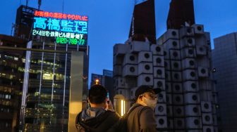 Orang-orang memotret Menara Kapsul Nakagin (kanan) di distrik Ginza, Tokyo, Jepang, Rabu (6/4/2022). [Philip FONG / AFP]