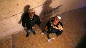 Dua orang Mesaharati menabuh gendang dan menyanyikan lagu-lagu religi sambil berkeliling membangunkan warga untuk sahur di Damaskus, Suriah, Kamis (7/4/2022). [LOUAI BESHARA / AFP]
