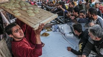 Pedagang membawa nampan berisi Qatayef (pangsit tradisional Arab) untuk pelanggan saat bulan Ramadhan di Gaza, Palestina, Minggu (3/4/2022). [Said Khatib / AFP]