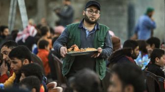 Seorang sukarelawan memberikan makanan kepada pengungsi Suriah selama jamuan buka puasa bersama saat bulan suci Ramadhan di Kota Al-Bab, provinsi Aleppo, Suriah, Kamis (7/4/2022). [Bakr ALKASEM / AFP]