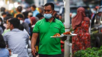 Pelayan mengantar makanan di Sentra kuliner Nasi Kapau di Jalan Kramat Raya, Senen, Jakarta Pusat, Selasa (12/4/2021). [Suara.com/Alfian Winanto]