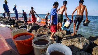 Sejumlah warga mengambil minyak solar yang tumpah dari kapal penggangkut Bahan Bakar Minyak (BBM) di Pelabuhan Depot Pertamina Desa Hagu Selatan, Lhokseumawe, Aceh, Minggu (24/4/2022). [ANTARA FOTO/Rahmad/foc]