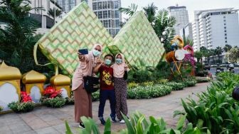 Warga berswafoto dengan latar belakang ornamen bernuansa lebaran yang terpasang di kawasan Bundaran HI, Jakarta Pusat, Selasa (26/4/2022). [Suara.com/Alfian Winanto]