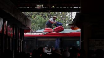 Kondektur merapikan barang bawaan penumpang di atas bus yang berhenti di Terminal Kampung Rambutan, Jakarta, Sabtu (30/4/2022). [Suara.com/Angga Budhiyanto]