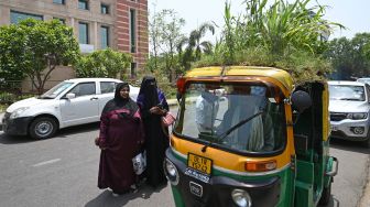 Orang-orang berbicara dengan pengemudi Bajaj Mahender Kumar saat dia duduk di kendaraannya di New Delhi, India, Senin (2/5/2022). [Money SHARMA / AFP]