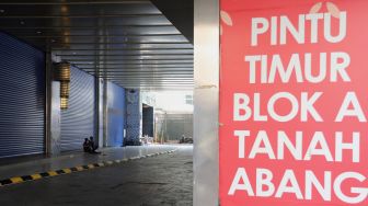Warga duduk di depan pintu masuk Pasar Tanah Abang Blok A, Jakarta, Kamis (5/5/2022). [Suara.com/Angga Budhiyanto]