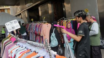 Pedagang pakaian melayani pembeli di depan pintu masuk Pasar Tanah Abang Blok A, Jakarta, Kamis (5/5/2022). [Suara.com/Angga Budhiyanto]