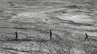 Warga berjalan melintasi sepetak dasar sungai Yamuna yang kering pada hari musim panas di New Delhi, India, pada (2/5/2022). [Sajjad HUSSAIN / AFP]