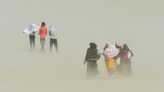 Warga berjalan di tengah badai pasir di Sangam, pertemuan sungai Gangga, Yamuna, dan Saraswati pada sore musim panas di Allahabad, India, pada (23/4/2022). [SANJAY KANOJIA / AFP]