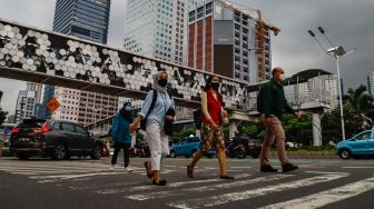 Sejumlah pekerja berjalan di pelican crossing saat jam pulang kerja di Jalan Sudirman, Jakarta Pusat, Senin (9/5/2022). [Suara.com/Alfian Winanto]