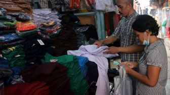 Pedagang seragam sekolah melayani calon pembeli di Pasar Jatinegara, Jakarta, Rabu (11/5/2022). [Suara.com/Angga Budhiyanto]