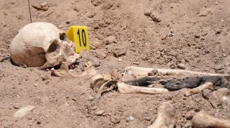 Tengkorak manusia yang digali dari kuburan massal tergeletak di tanah di Kota Najaf, Irak, Sabtu (14/5/2022). [AFP]