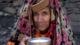 Seorang wanita suku Kalash yang mengenakan pakaian tradisional minum susu sebagai bagian dari ritual pada hari pertama festival &#039;Joshi&#039; di desa Bumburet, Pakistan, Sabtu (14/5/2022). [Abdul MAJEED / AFP]
