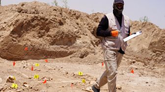 Seorang ahli forensik bekerja di kuburan massal di mana sisa-sisa tengkorak manusia digali di Kota Najaf, Irak, Sabtu (14/5/2022). [AFP]
