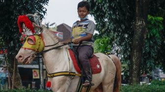 Seorang anak berwisata sambil menunggangi kuda di kawasan Kanal Banjir Timur (KBT), Jakarta Timur, Senin (16/5/2022). [Suara.com/Alfian Winanto] 