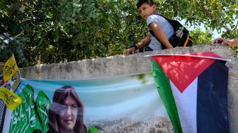 Seorang anak laki-laki duduk di dinding yang menghadap ke pameran seni untuk menghormati mendiang jurnalis Al-Jazeera Palestina, Shireen Abu Akleh di kota Jenin, Palestina, Kamis (19/5/2022). [RONALDO SCHEMIDT / AFP]