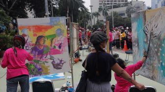 Seniman yang tergabung dalam Perempuan Perupa Indonesia melukis dan menggelar pameran bersama di depan Pos Polisi Thamrin, Jakarta, Minggu (22/5/2022). [Suara.com/Angga Budhiyanto]